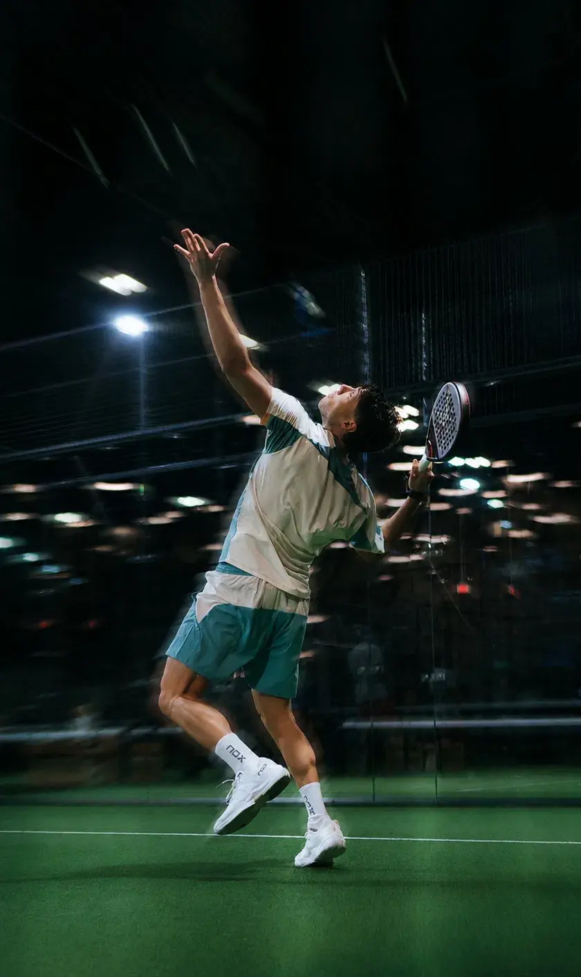 Padel player reaching up for an overhead on an indoor court
